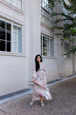 Tiered floral maxi dress with smocked bodice and balloon sleeves, worn by woman near a building with tall windows