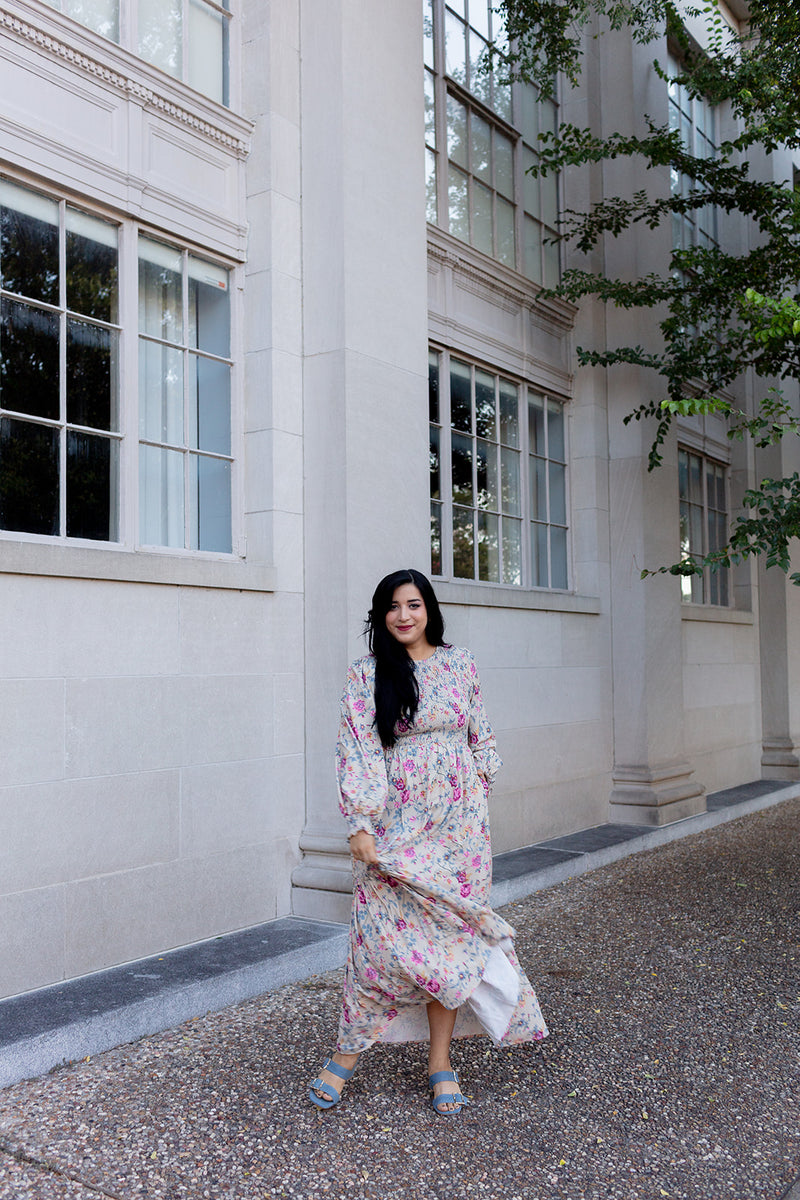 Tiered floral maxi dress with smocked bodice and balloon sleeves, worn by woman near a building with tall windows