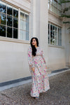 Boho-style cream maxi dress with colorful floral pattern and ruffle details, worn outside urban architecture
