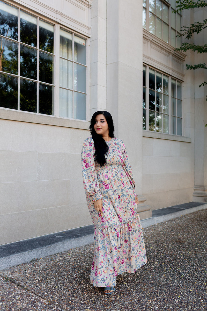 Boho-style cream maxi dress with colorful floral pattern and ruffle details, worn outside urban architecture
