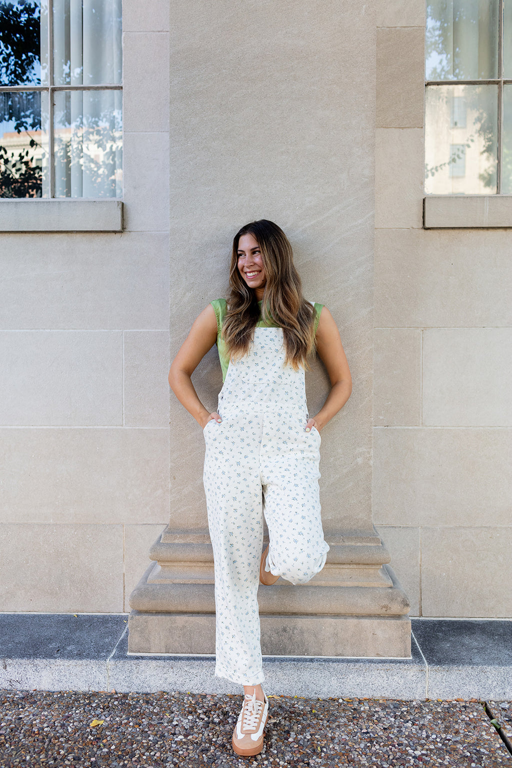Woman in a white floral overalls standing on steps outside a building.