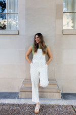 Woman in a white floral overalls standing on steps outside a building.