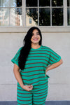 Woman wearing a green and brown striped outfit standing against a light-colored wall.