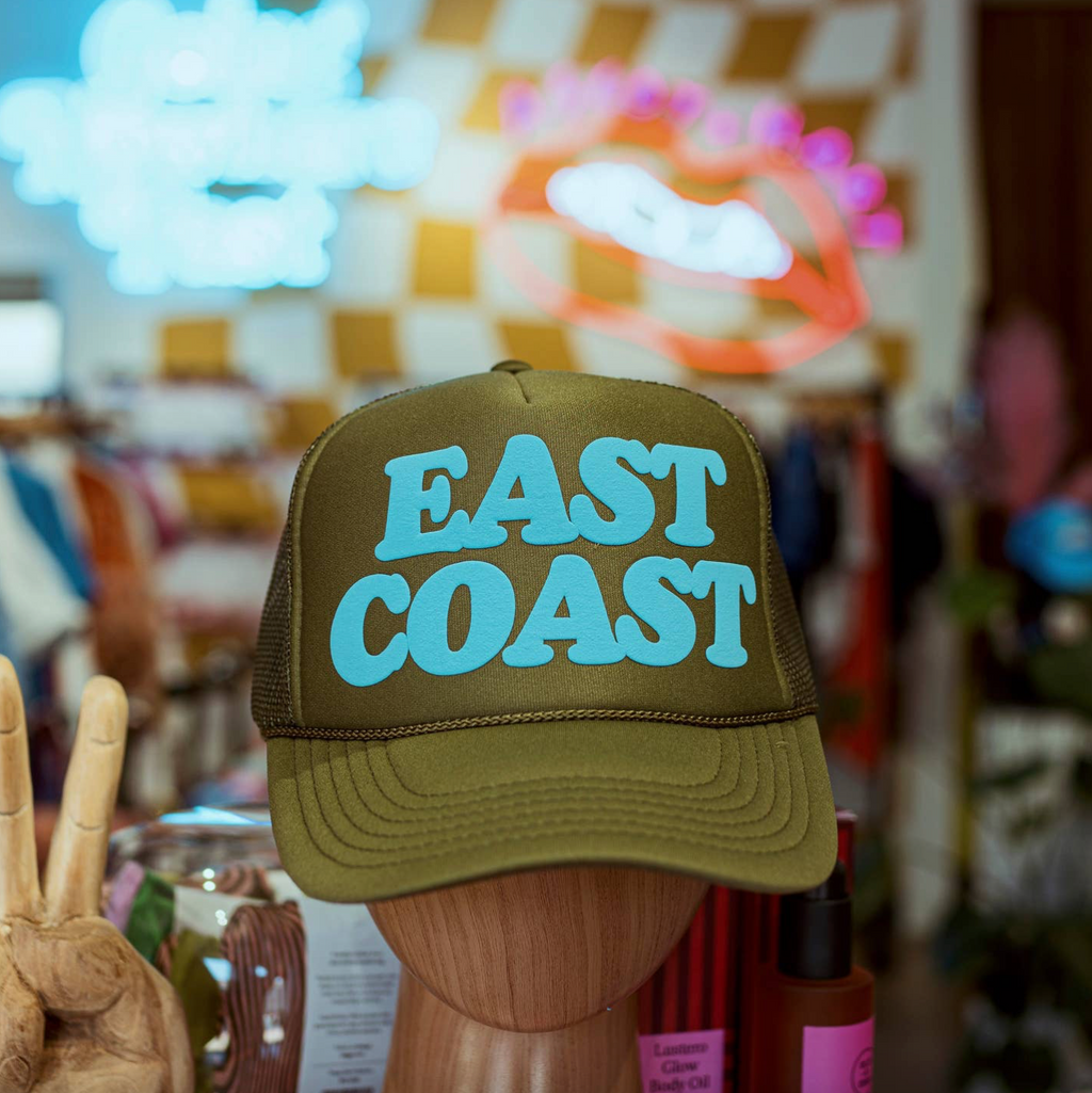 Green cap with 'East Coast' text on a wooden stand against a colorful, blurred background