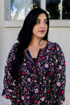 Woman wearing a floral blouse standing against a neutral background