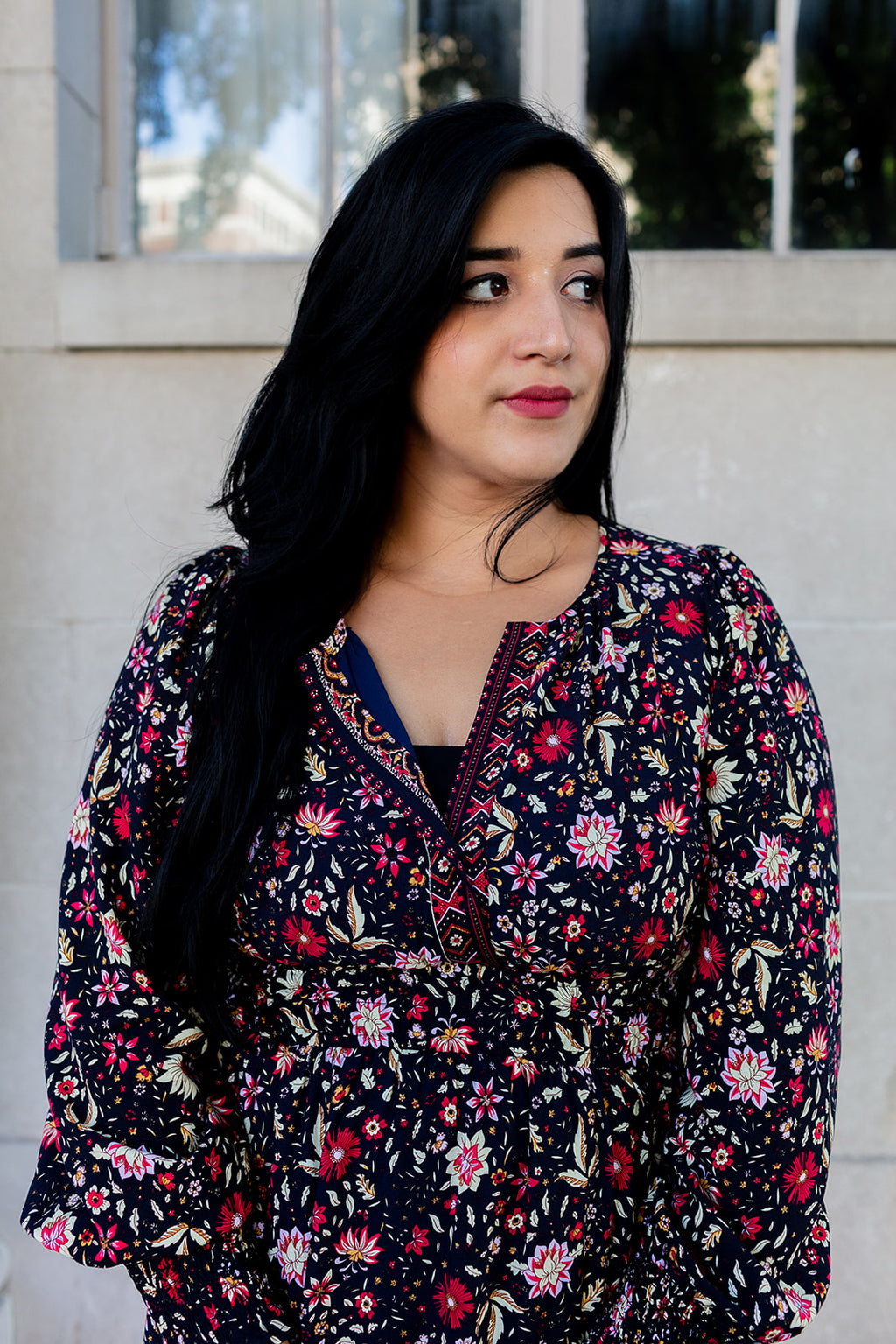Woman wearing a floral blouse standing against a neutral background