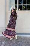 Woman in a floral dress standing outside a building with large windows.