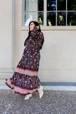 Woman in a floral dress standing outside a building with large windows.
