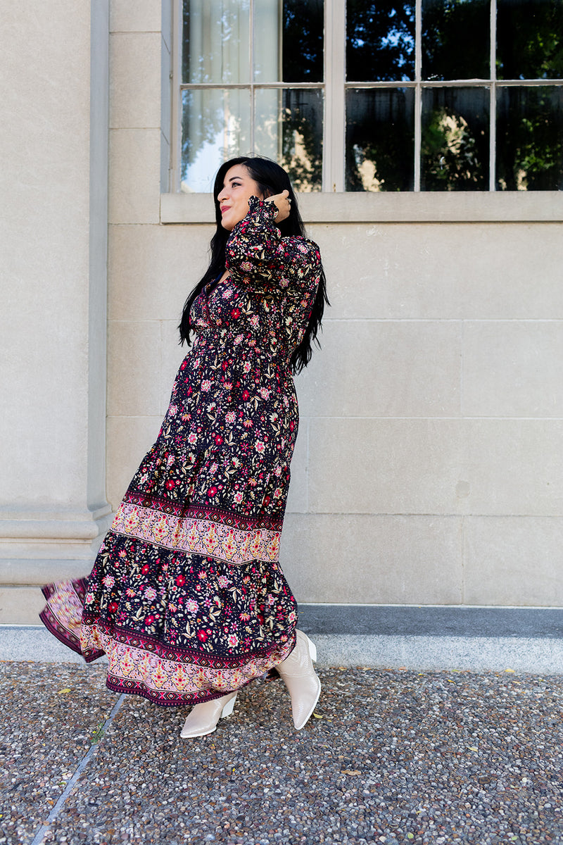 Woman in a floral dress standing outside a building with large windows.