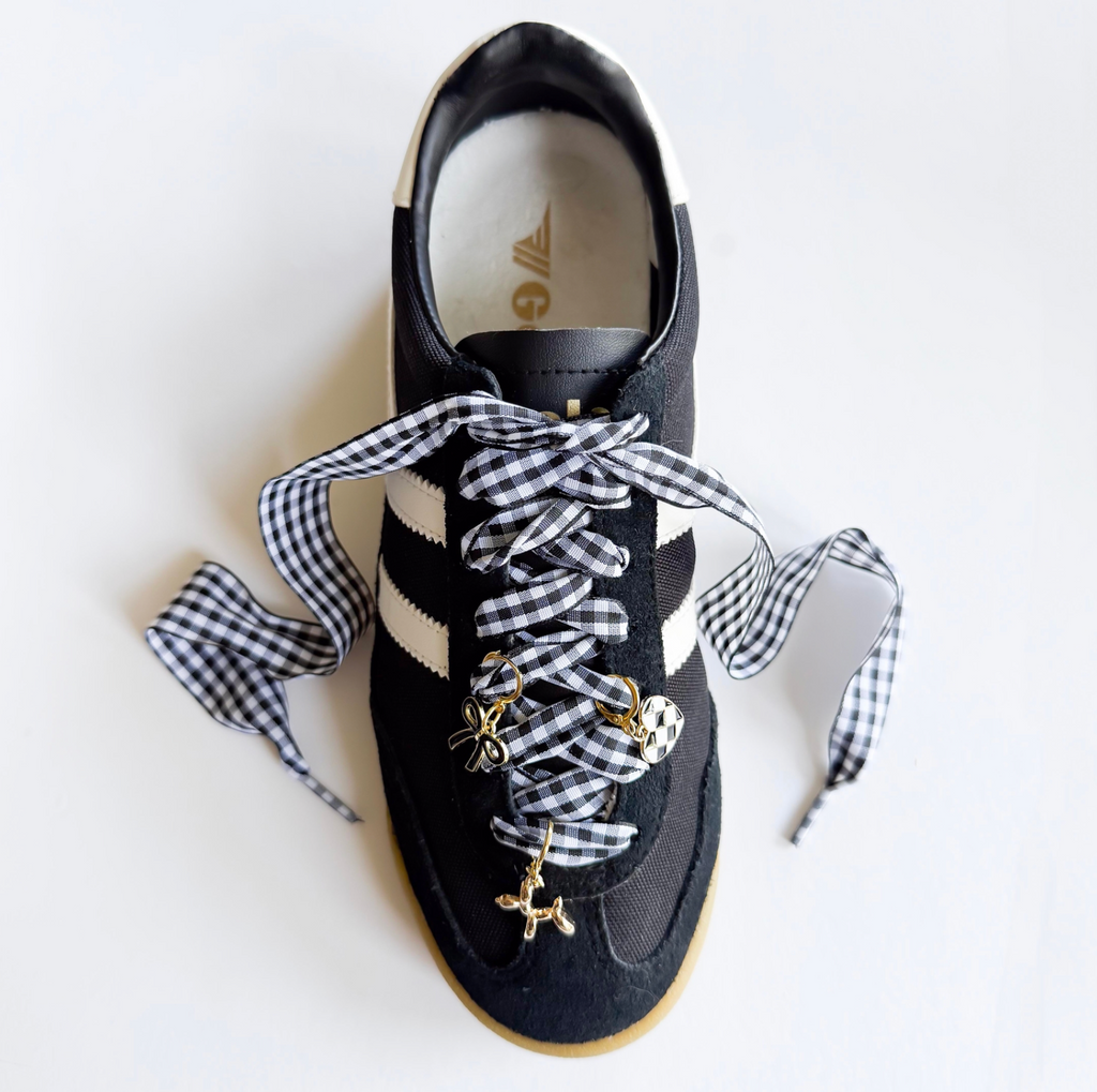 Black sneaker with checkered laces and gold charms on a white background