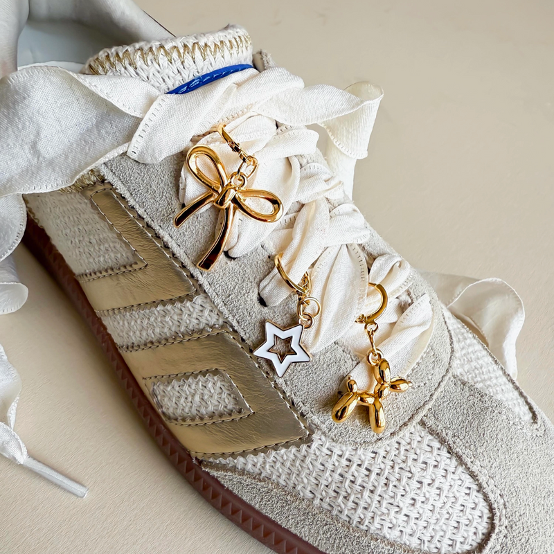 A trio of playful gold charms 🌟🎀 featuring a bow, star, and balloon dog, clipped onto white sneaker laces.