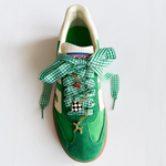 Green sneaker with checkered laces and decorative charms on a white background