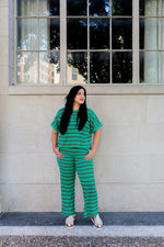 Woman in a green striped outfit standing in front of a building with large windows.