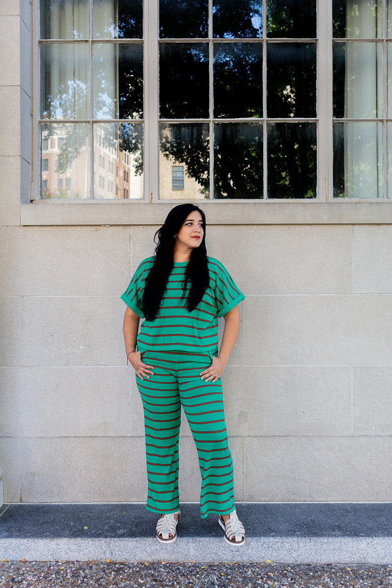Woman in a green striped outfit standing in front of a building with large windows.