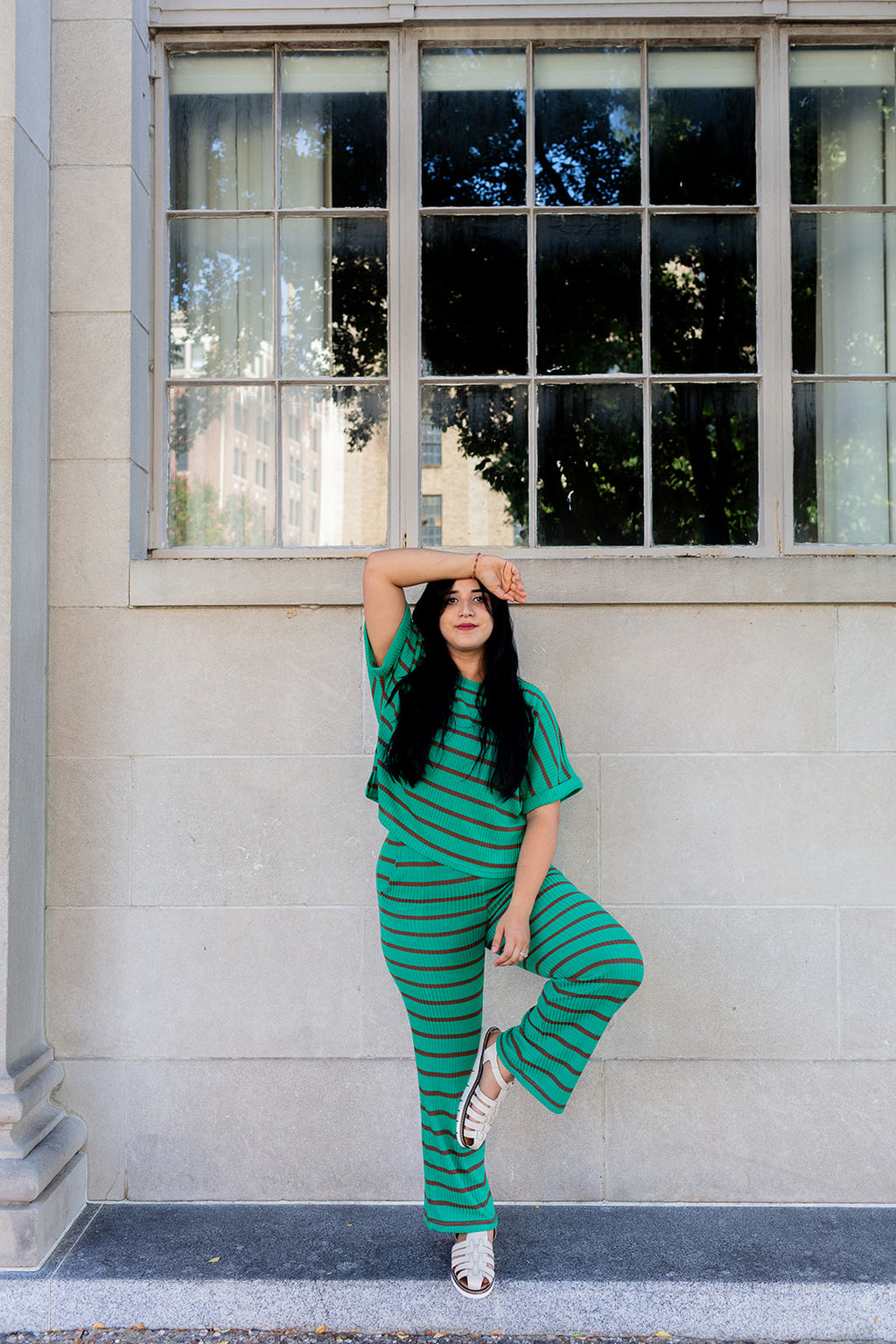 Woman in a green striped outfit posing against a building with large windows.