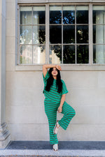 Woman in a green striped outfit posing against a building with large windows.