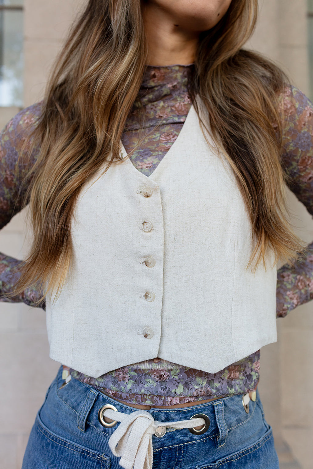 Person wearing a white vest over a floral shirt with blue pants.
