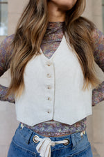Person wearing a white vest over a floral shirt with blue pants.
