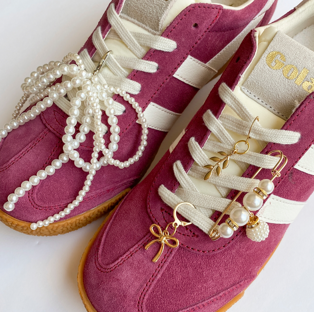 Pink sneakers with decorative laces featuring pearls and gold bows on a white background