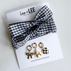 Black and white checkered headband with three gold earrings on a white card featuring 'Leo + Lee' brand.