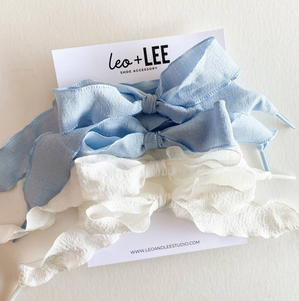 Two shoe accessories, one blue and one white, with 'Leo + Lee' branding on a light background.