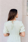 Woman wearing a light green dress standing against a beige wall.