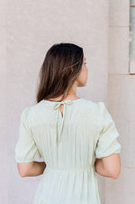 Woman wearing a light green dress standing against a beige wall.