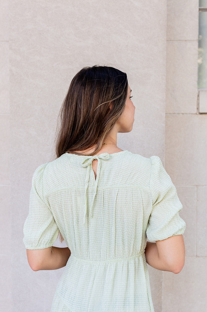 Woman wearing a light green dress standing against a beige wall.