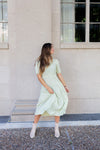 Woman in a light green dress standing against a stone building.