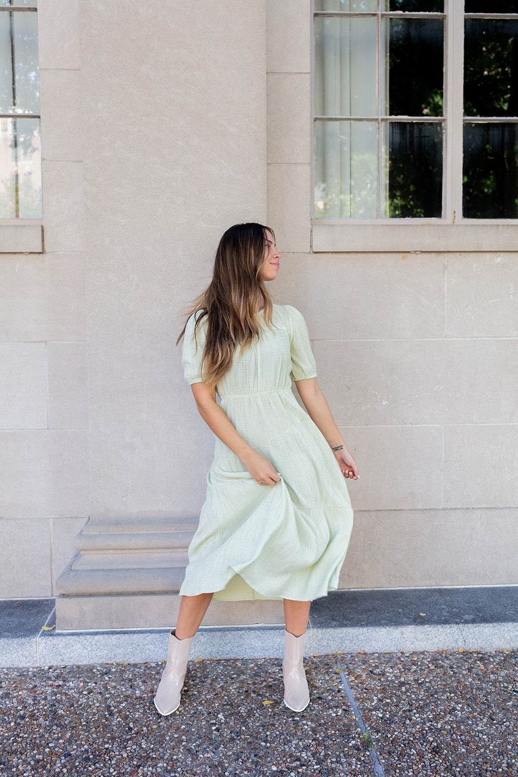 Woman in a light green dress standing against a stone building.