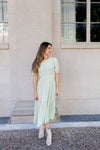 Woman in a light green dress standing outside a building.