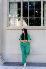 Woman in green striped outfit leaning against a building with large windows.